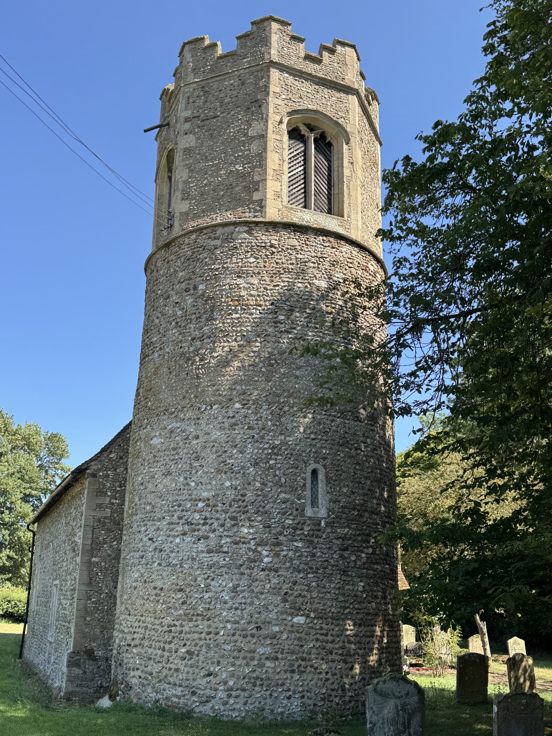The round tower of All Saints Little Bradley rising above the churchyard.