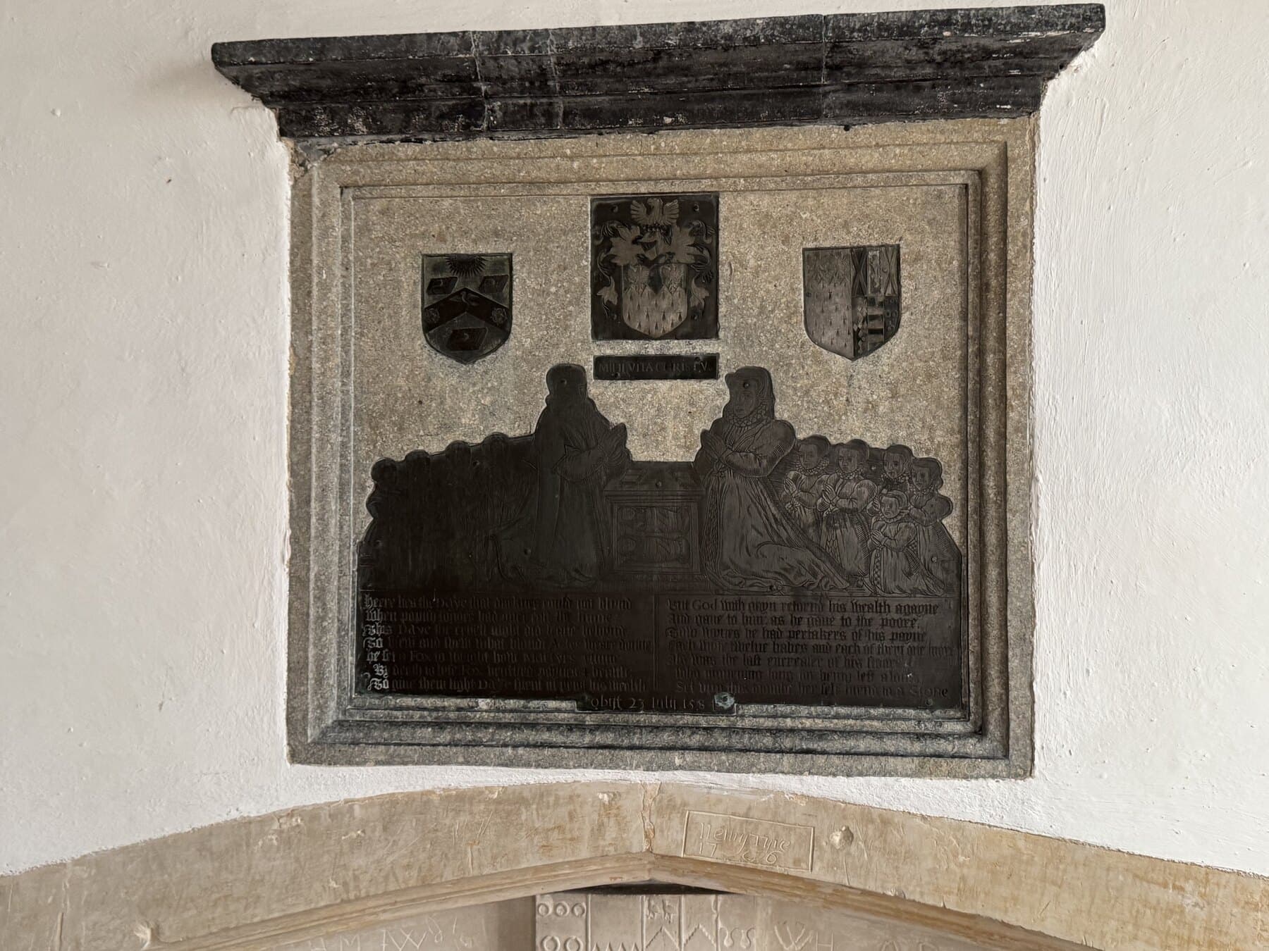 John and Alice Daye memorial brass on the north chancel wall, showing the couple kneeling at a prayer desk with their children beneath three shields.